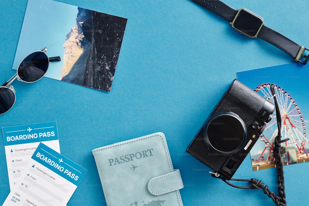 un passeport, des lunettes de soleil, un appareil photo et d’autres articles disposés sur une surface bleue