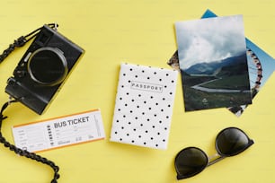 Reisepass, Sonnenbrille, Kamera und ein Ticket auf gelbem Hintergrund