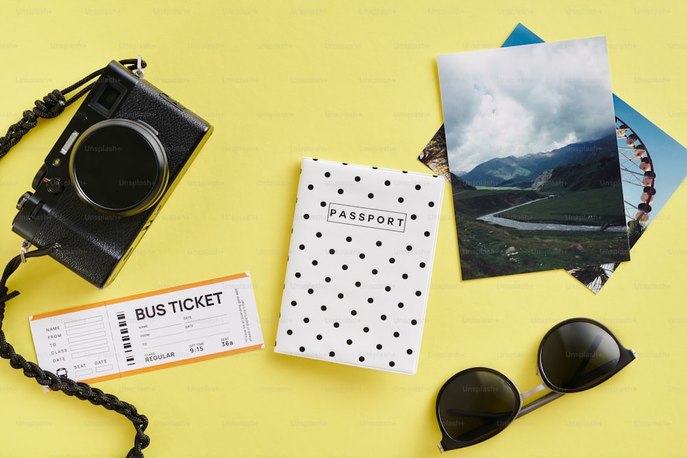 um passaporte, óculos escuros, câmera fotográfica e um bilhete em um fundo amarelo