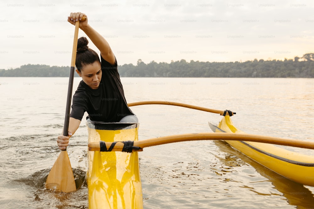 a woman in a black shirt paddling a yellow kayak