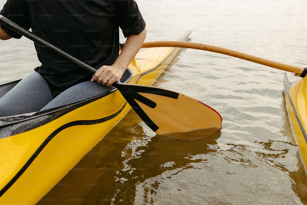 a man in a black shirt is paddling a yellow kayak