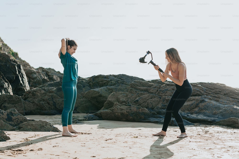 duas mulheres em pé em uma praia com uma câmera