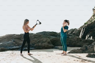 Dos mujeres de pie en una playa sosteniendo una cámara