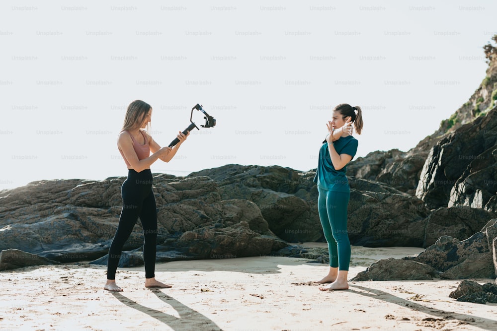 two women standing on a beach holding a camera