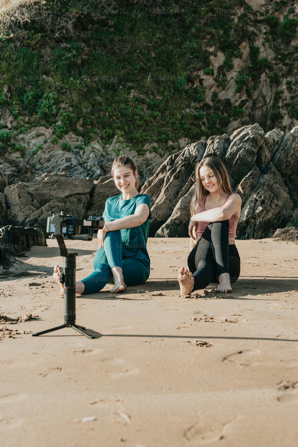 a couple of girls sitting on top of a sandy beach