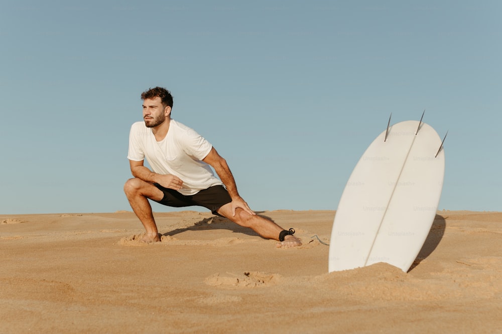 a man kneeling down next to a surfboard in the sand