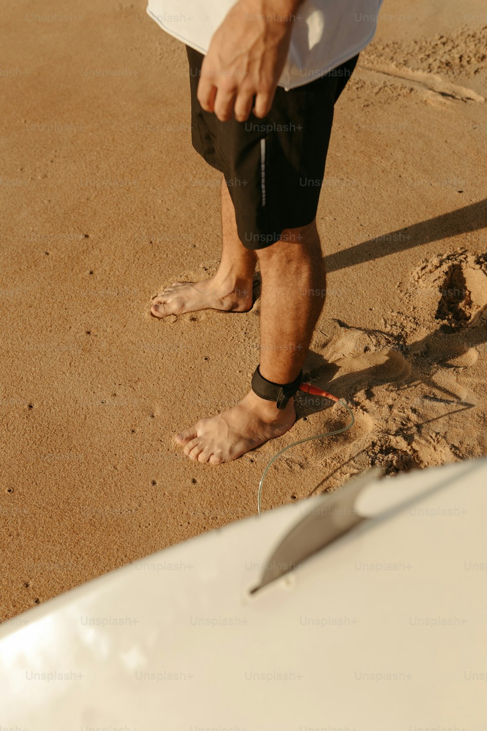 a man standing in the sand next to a surfboard