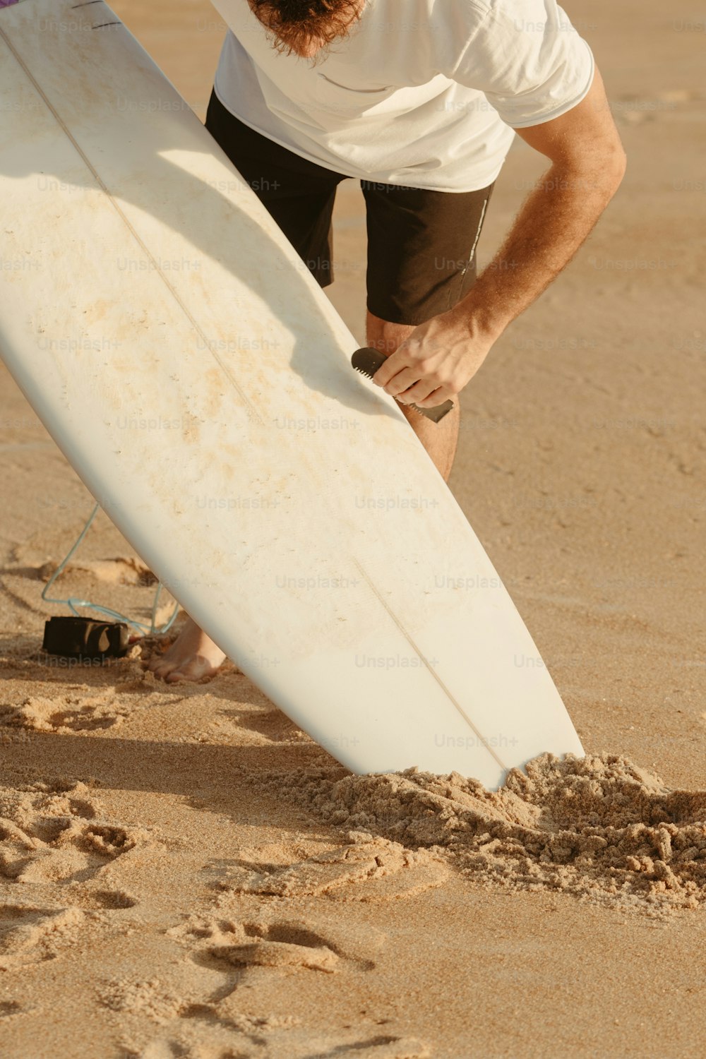 um homem segurando uma prancha de surf em uma praia de areia