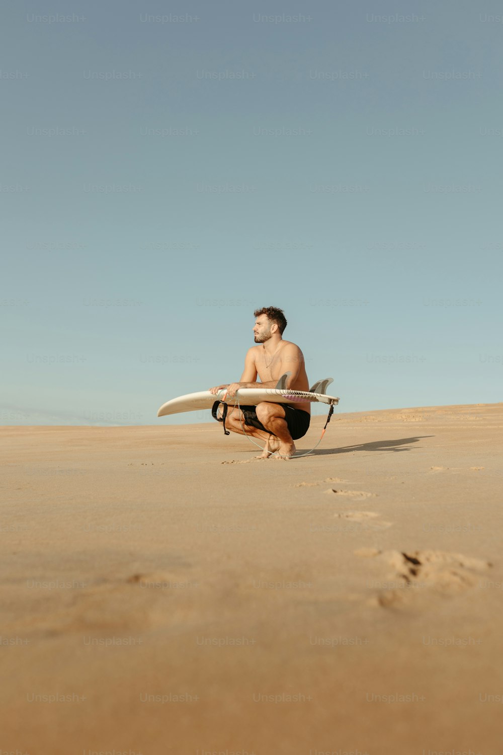 Un hombre arrodillado mientras sostiene una tabla de surf