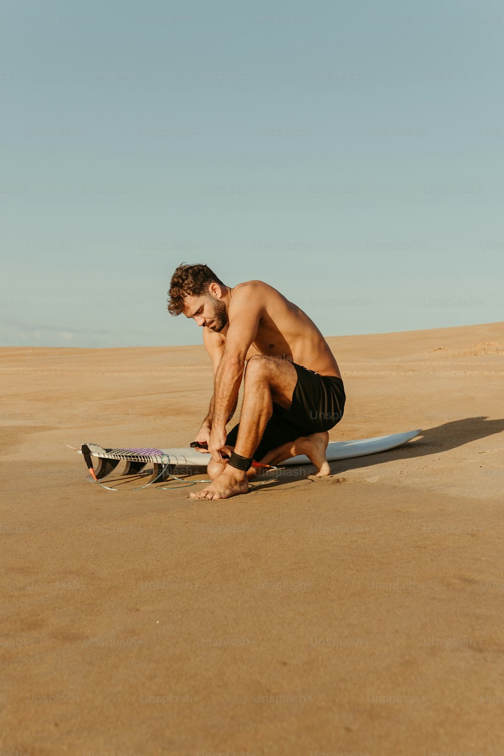 Un uomo inginocchiato su una spiaggia accanto a una tavola da surf