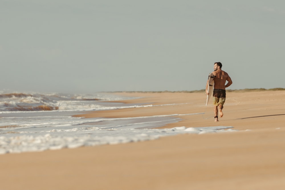 um homem correndo na praia com uma prancha de surf;