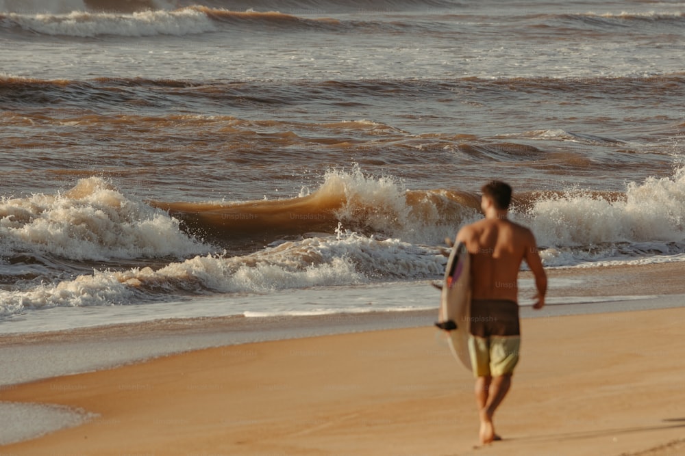 ein mann, der mit einem surfbrett am strand spazieren geht