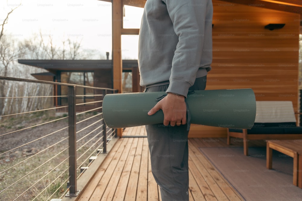 um homem segurando um tapete de ioga em um deck