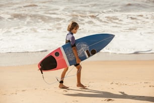 a young boy carrying a surfboard on a beach