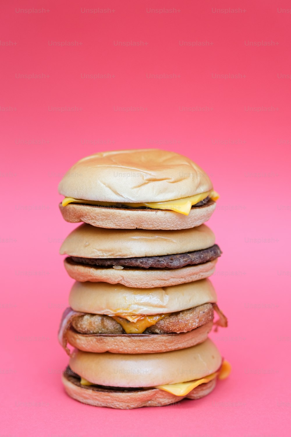 Una pila de hamburguesas sobre un fondo rosa