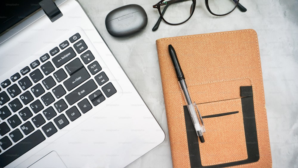 a notebook with a pen, glasses, eyeglasses and a laptop on a