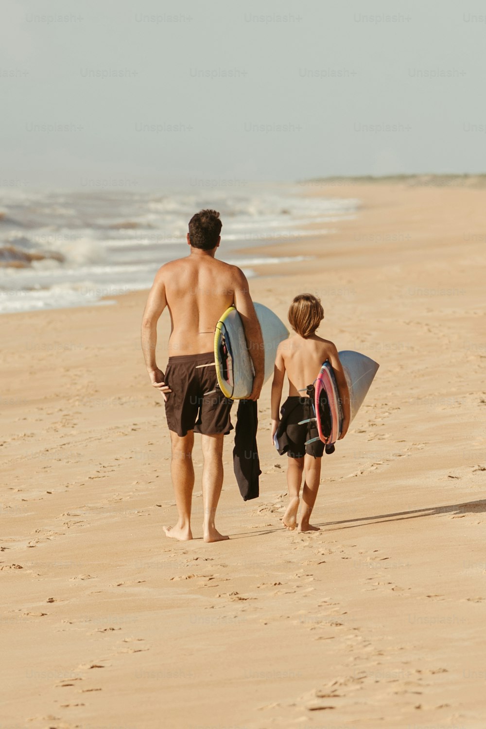 a man and a boy walking on the beach with surfboards