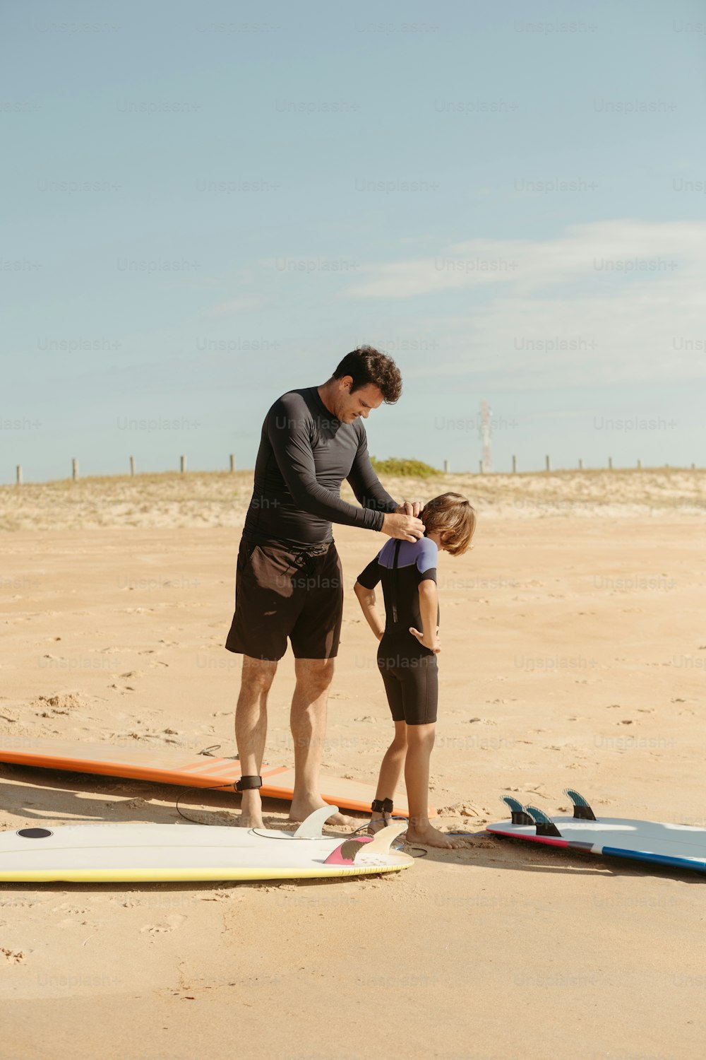 Un homme et une petite fille debout sur une plage à côté de planches de surf