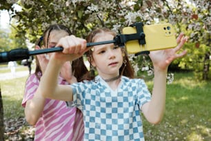 two young girls looking through binoculars at a tree