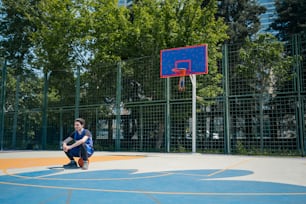 Ein junger Mann, der auf einem Basketballplatz vor einem Basketballkorb sitzt