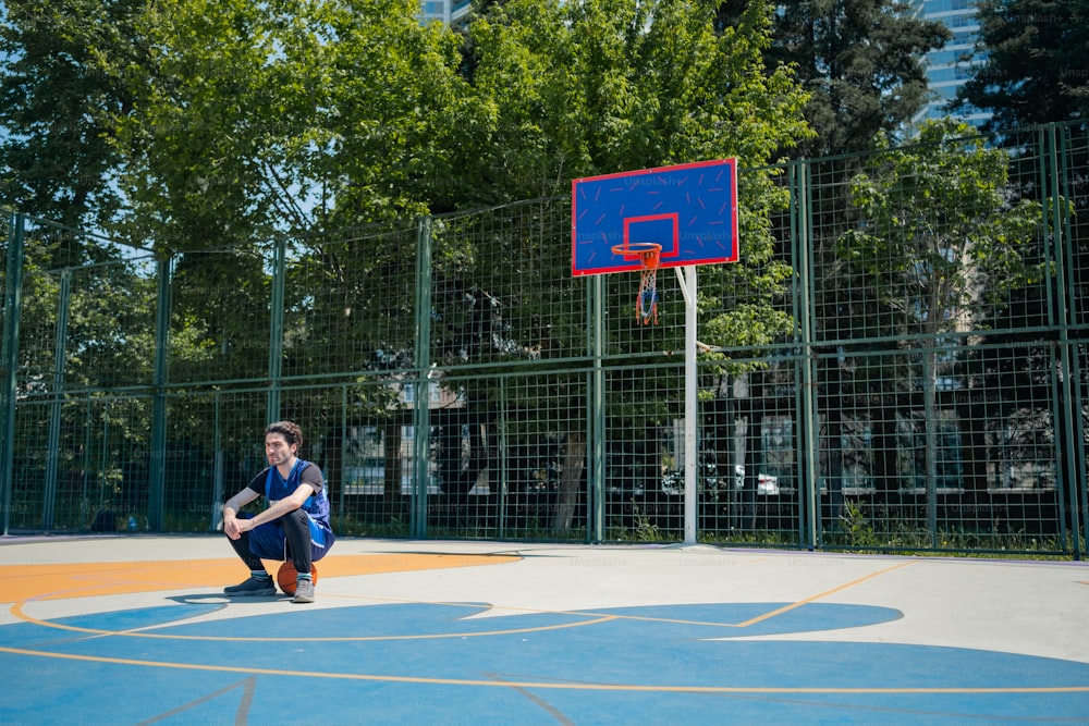 a young man sitting on a basketball court in front of a basketball hoop