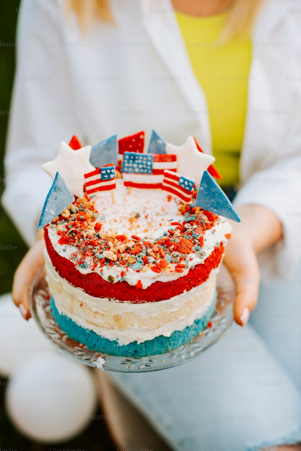 Una mujer sosteniendo un pastel con glaseado rojo, blanco y azul