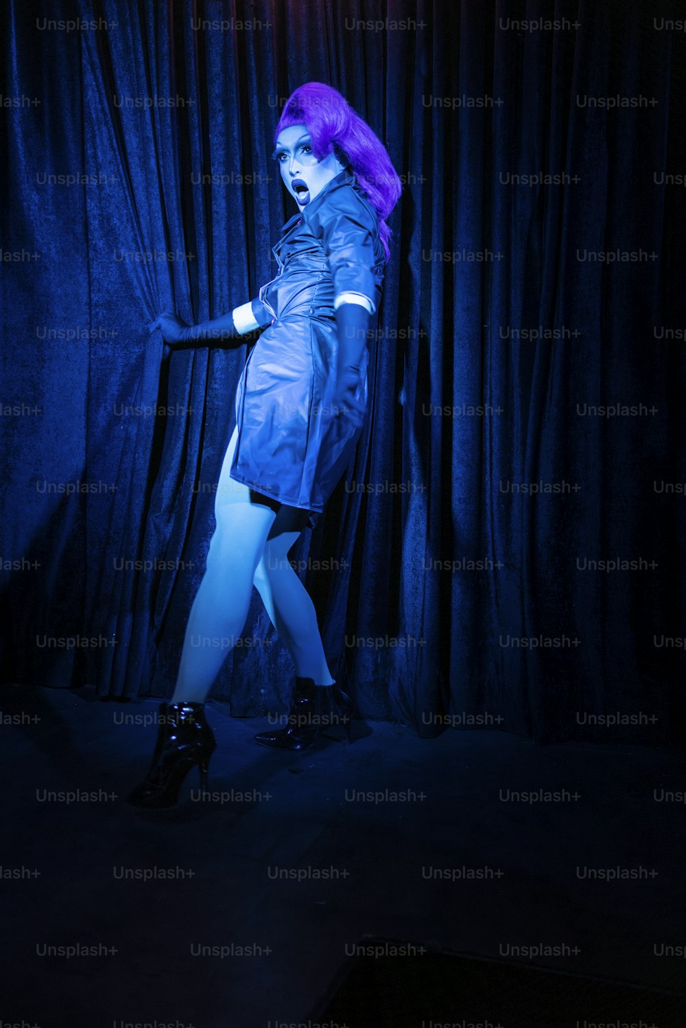 a woman with purple hair is standing in front of a curtain