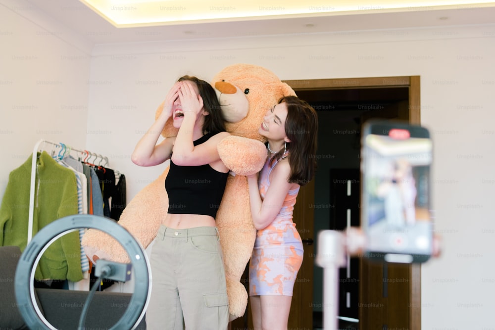 Duas meninas segurando um grande urso de pelúcia em um quarto