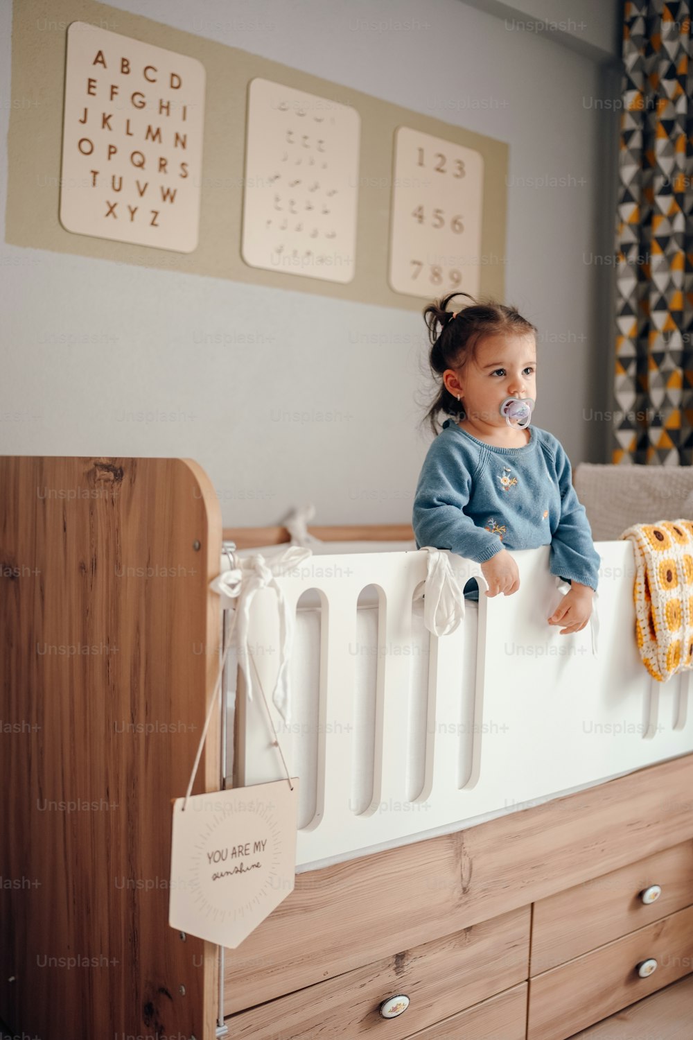 ein kleines Mädchen, das mit einem Schnuller im Mund auf einem Kinderbett steht