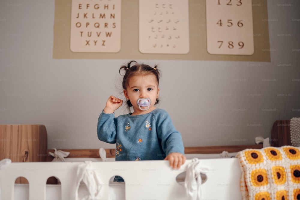 a little girl standing in a crib with a pacifier in her mouth