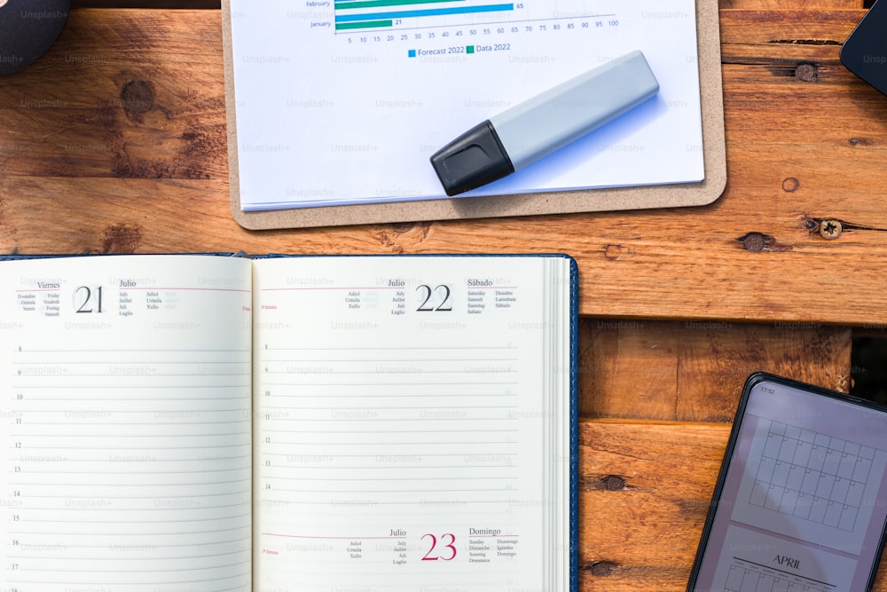 a desk with a notebook, pen, cell phone and a calendar