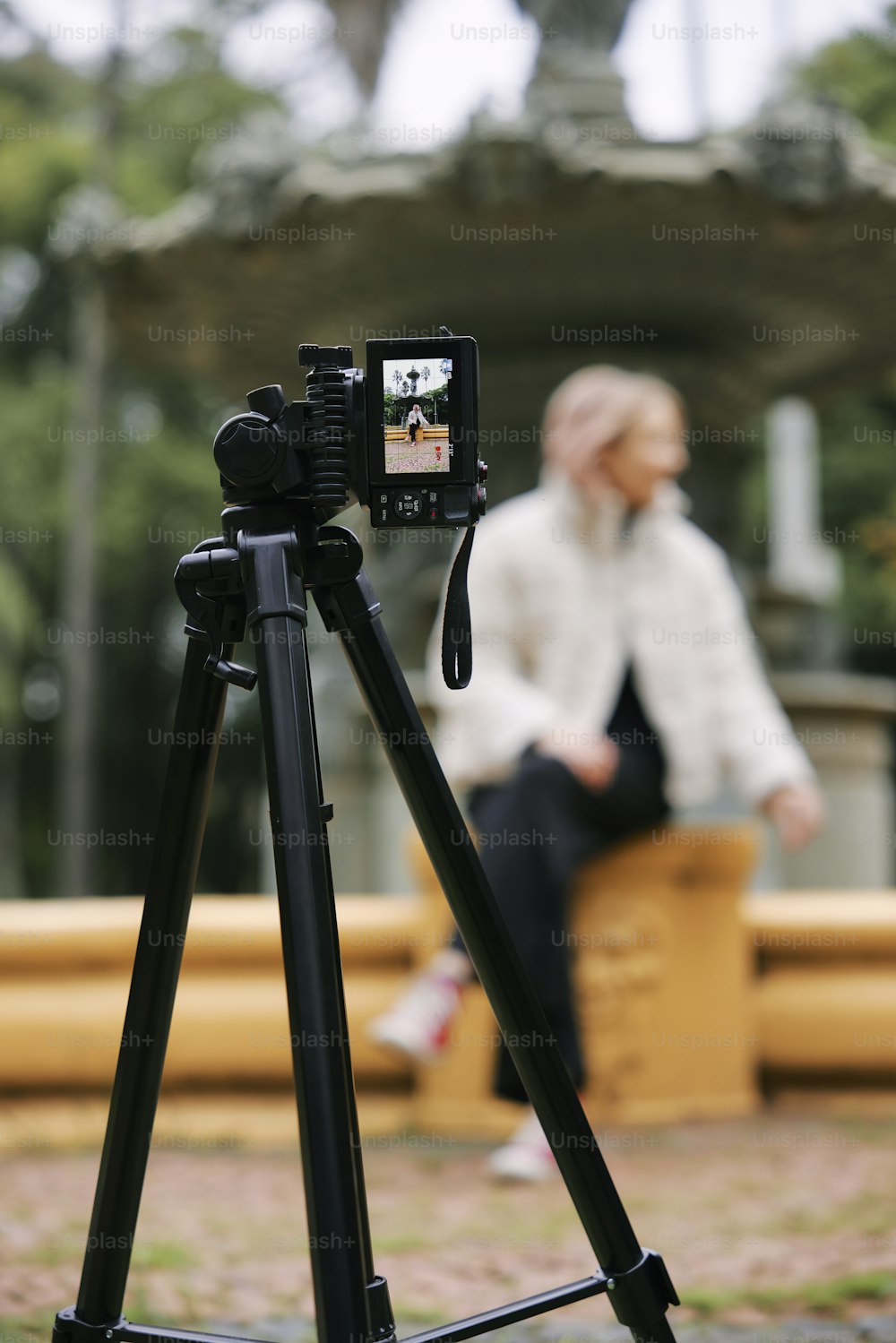 eine Person, die mit einer Kamera auf einem Stativ auf einer Bank sitzt