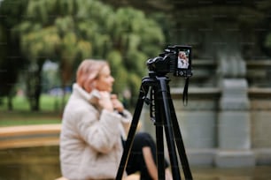 a woman sitting on a bench with a camera on a tripod