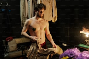 a shirtless man standing next to a pile of clothes