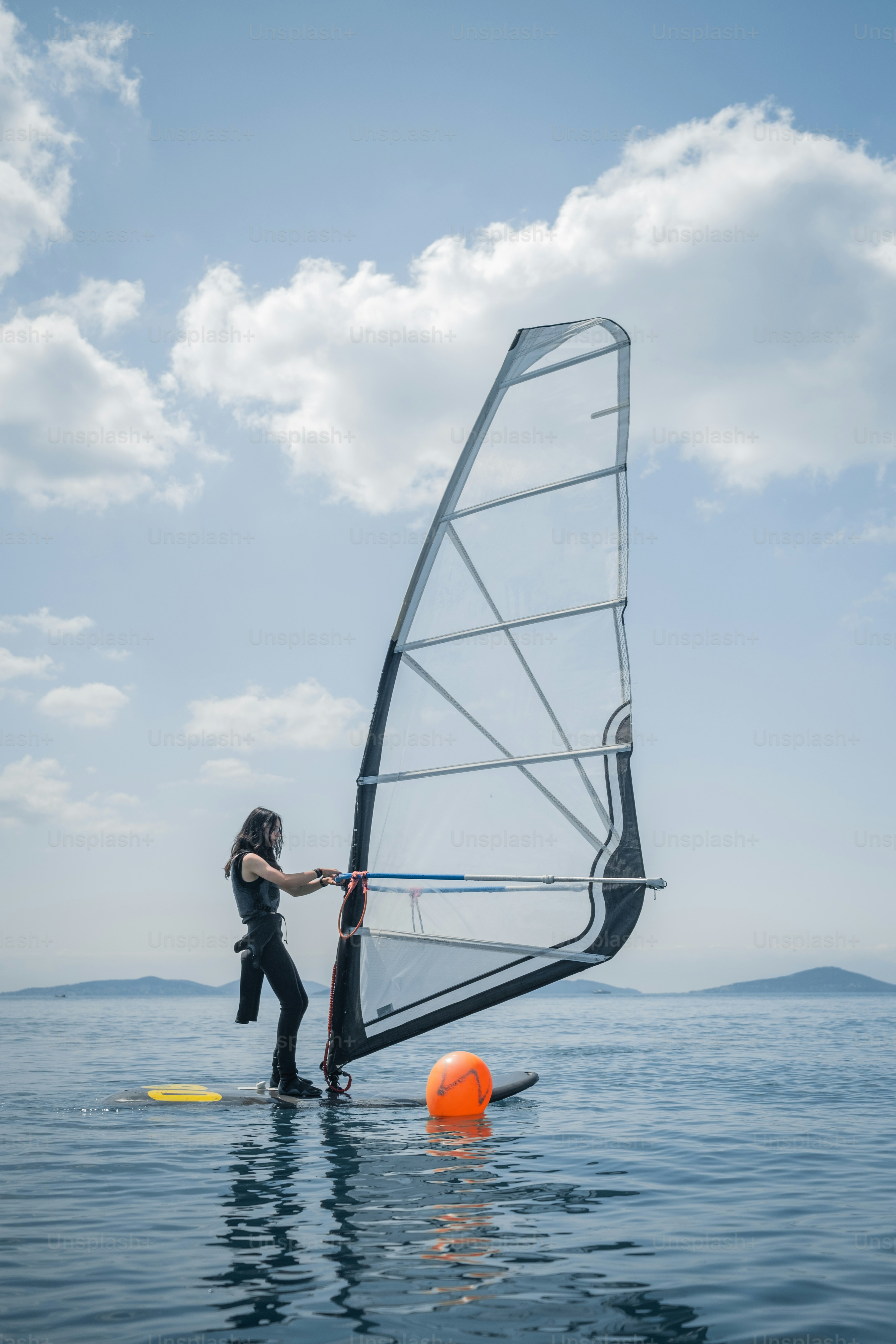 Frau Windsurft auf einem ruhigen, blauen Meer unter bewölktem Himmel