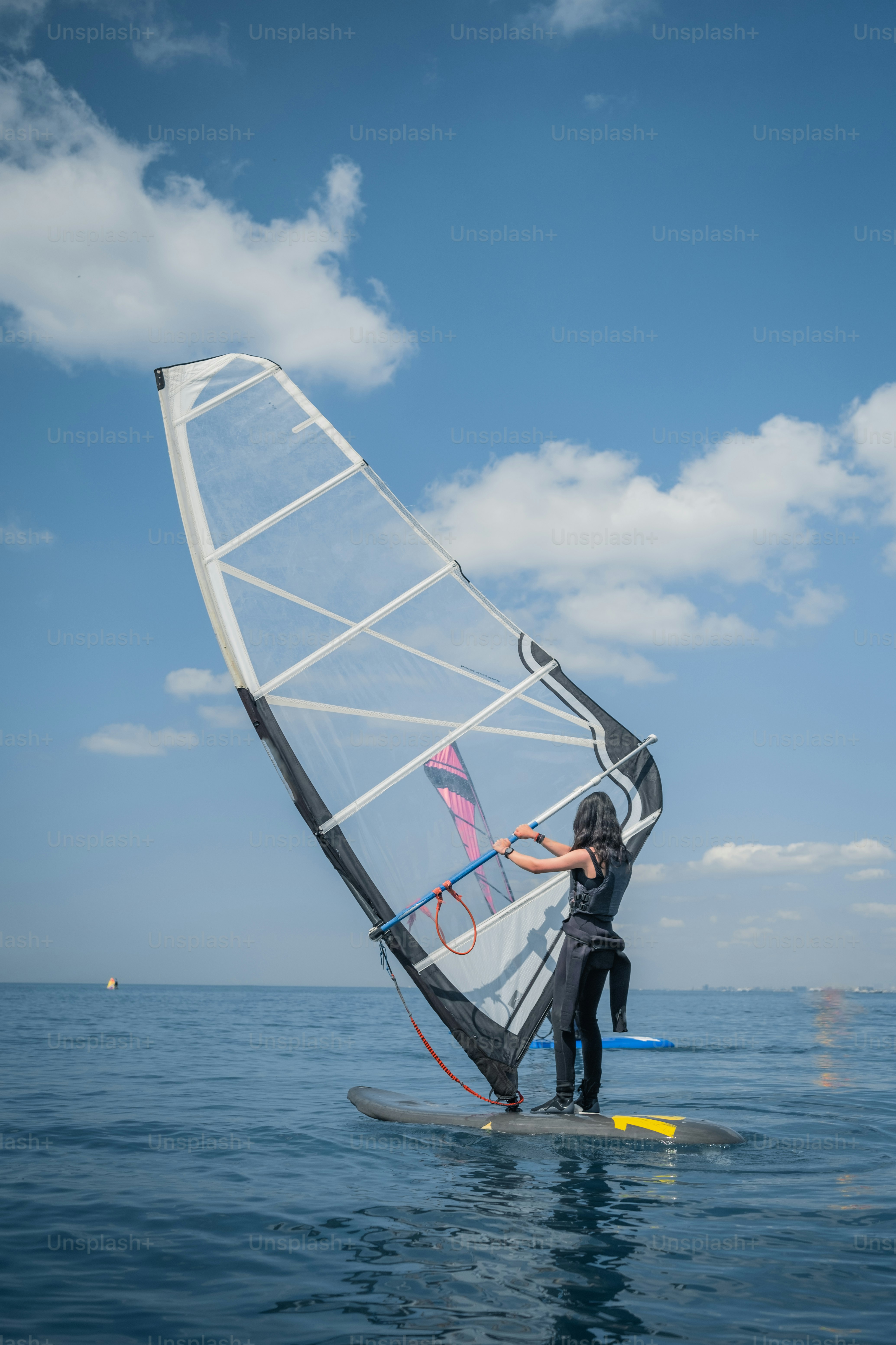 Eine Person, die auf einem ruhigen, blauen Meer Windsurfen fährt.