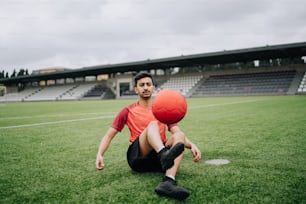 Un hombre sentado en el suelo sosteniendo una pelota roja