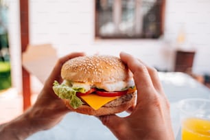 a person holding a hamburger with cheese and lettuce