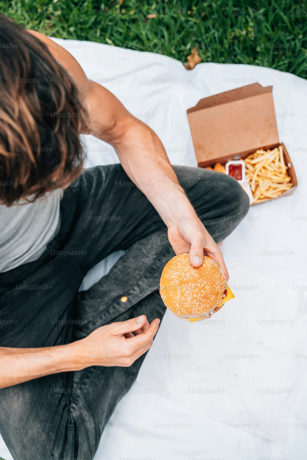 Un hombre sentado en una manta sosteniendo una hamburguesa