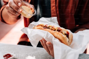 una persona seduta a un tavolo che mangia un hot dog