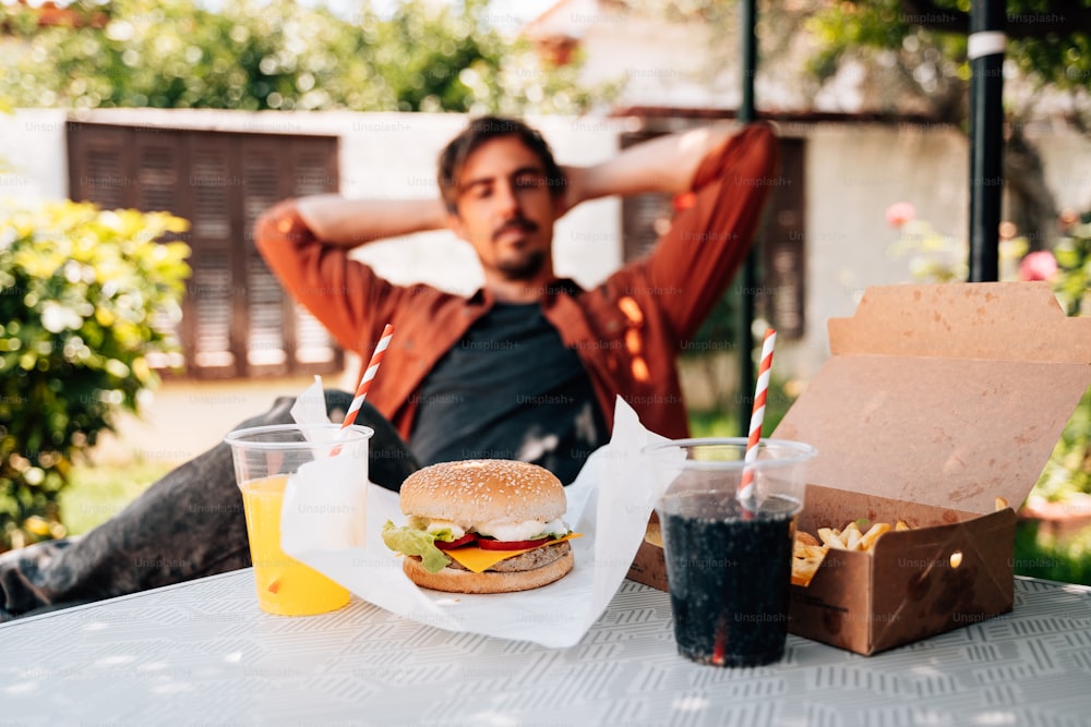 a man sitting at a table with a burger and drinks