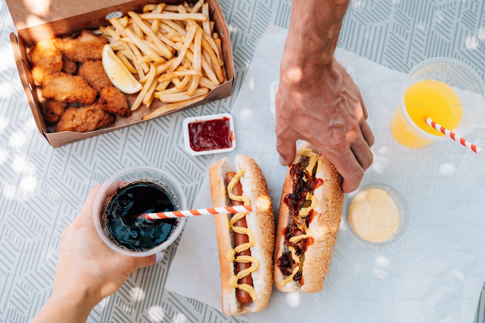 una persona che tiene un hot dog accanto a una scatola di patatine fritte e ketchup