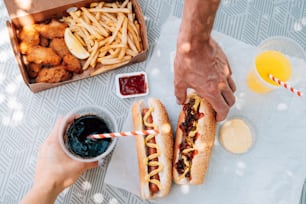 une personne tenant un hot-dog à côté d’une boîte de frites et de ketchup