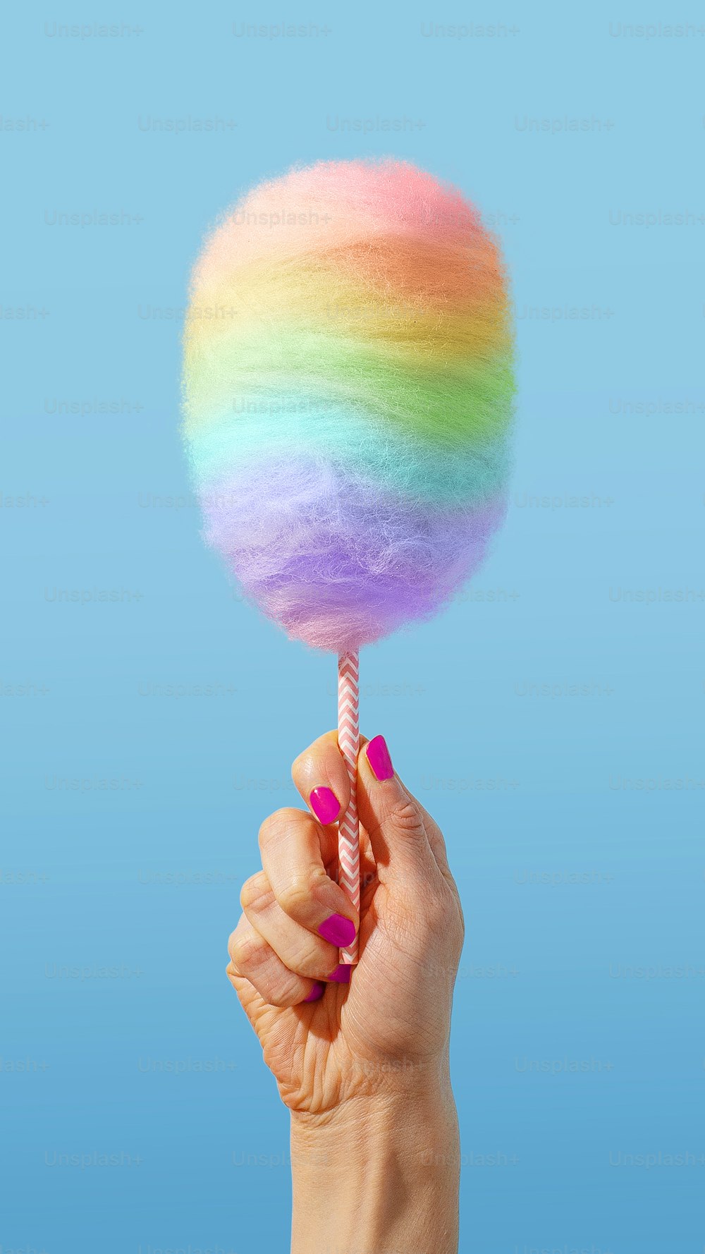 Una mano sosteniendo una piruleta arco iris en un palo