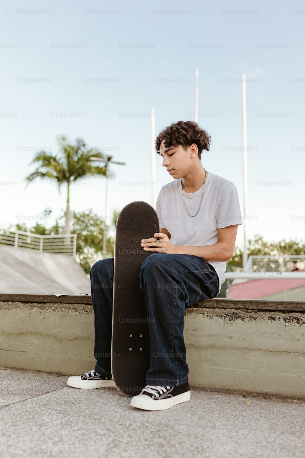Un jeune homme assis sur un rebord tenant une planche à roulettes