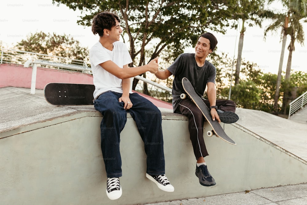 Dos jóvenes sentados en una repisa con patinetas