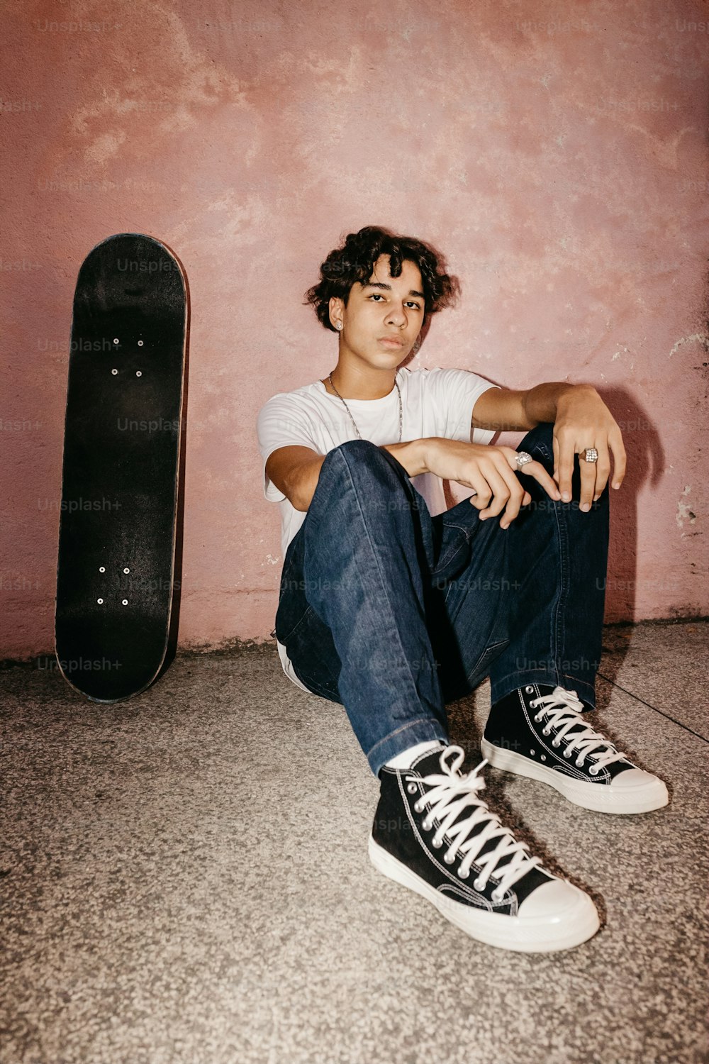 a young man sitting on the floor next to a skateboard
