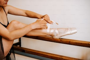 Una mujer está sentada en un banco atando sus zapatos de ballet