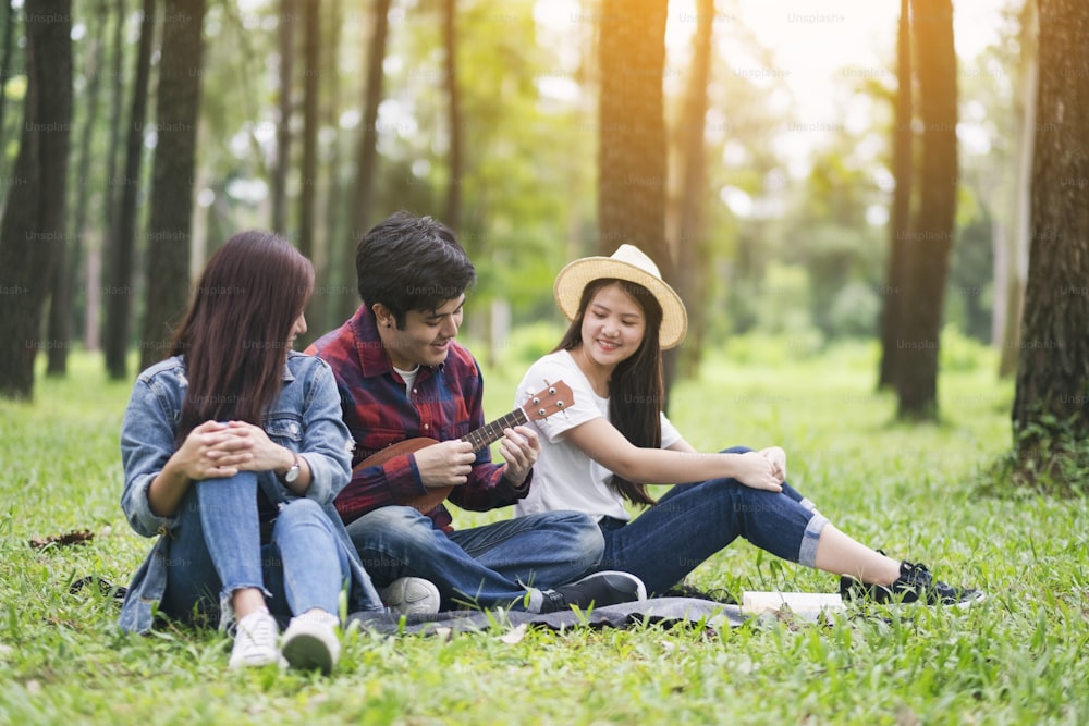 A group of young people playing ukulele while sitting together in the park