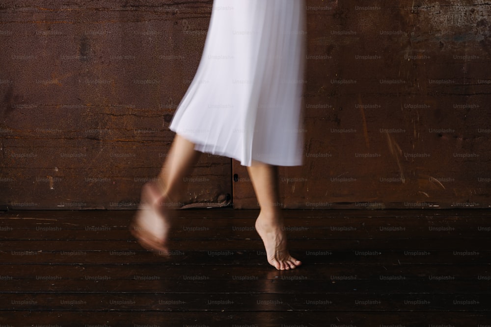 a woman in a white dress walking across a wooden floor
